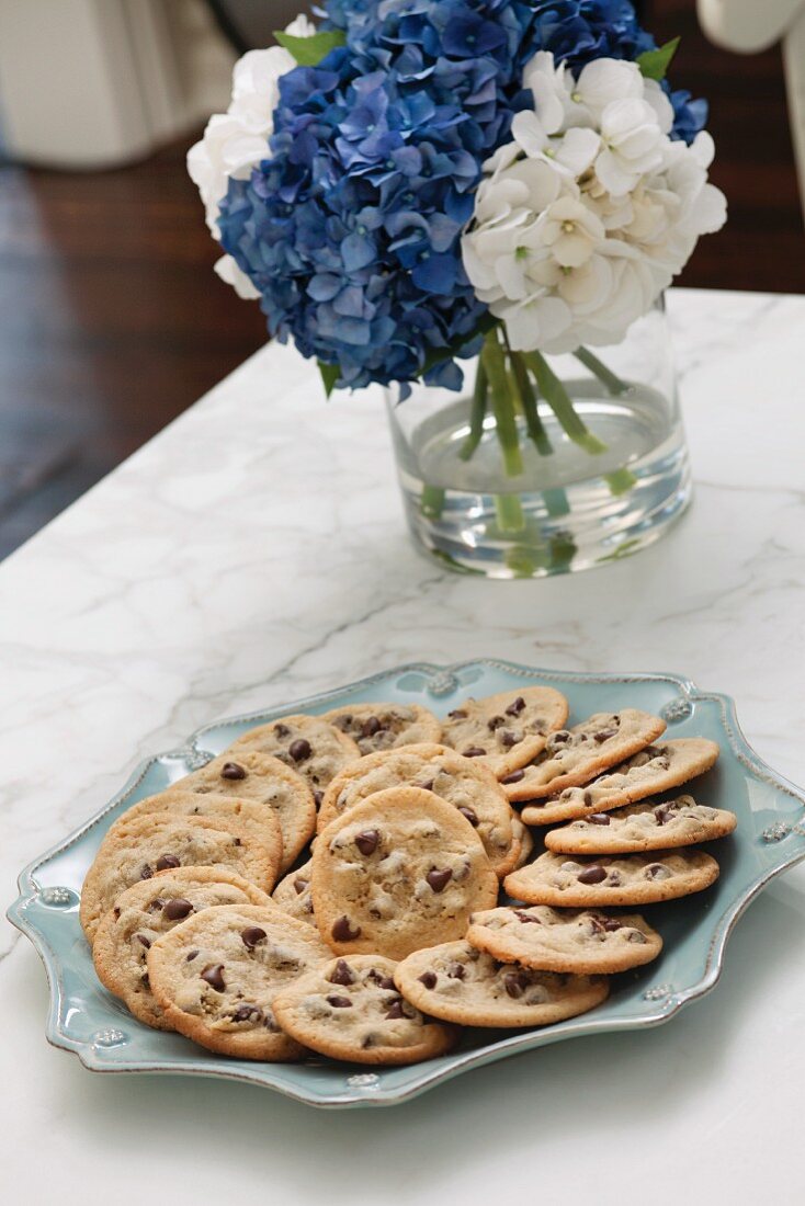 Chocolate chip cookies on a plate with a bunch of hydrangeas in the background