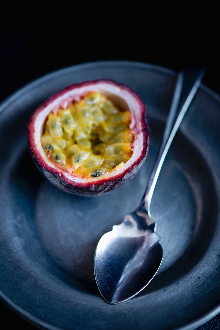 Half a passion fruit on a pewter plate with a silver spoon