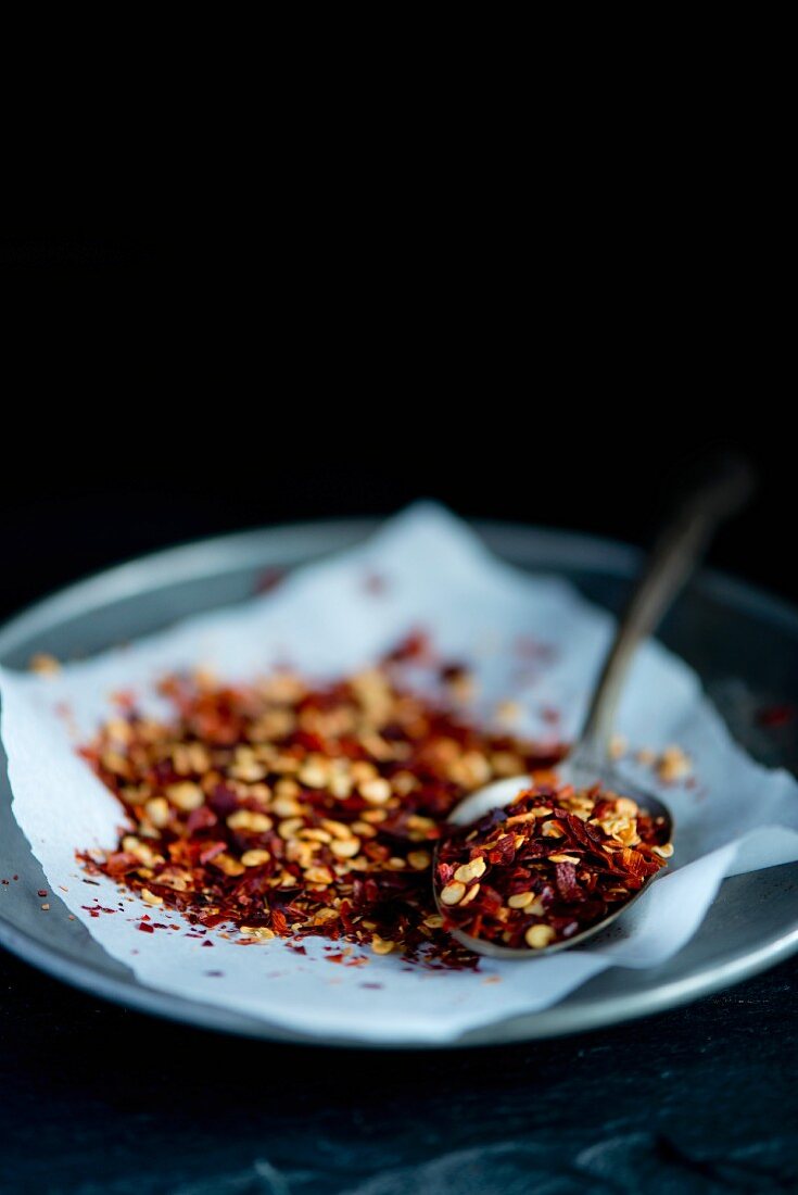 Red Italian chilli flakes on a pewter plate on a white piece of paper