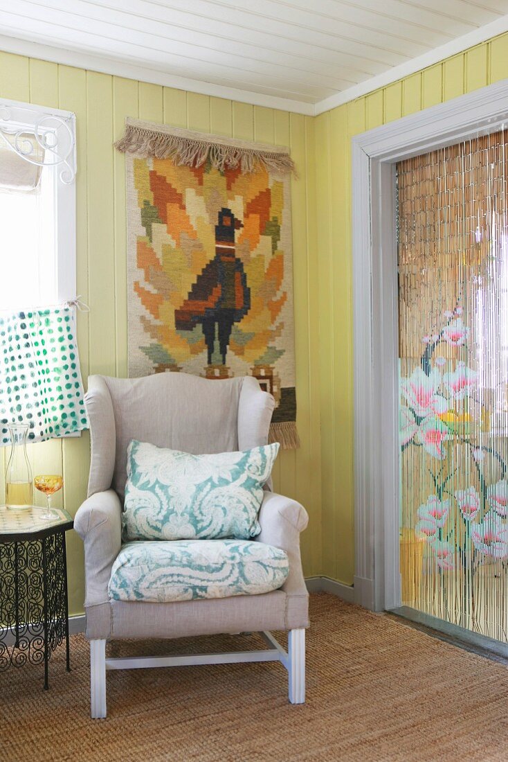 Wing-back chair below tapestry on board wall and next to Oriental bead curtain