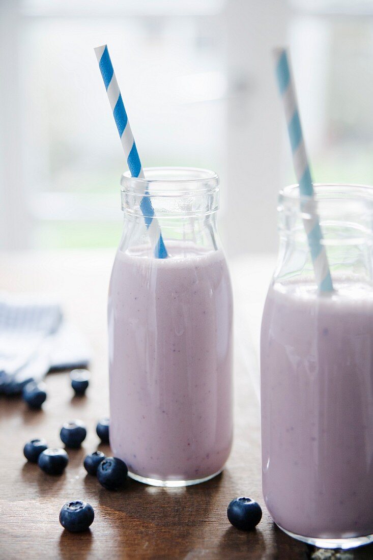Two bottles of blueberry and banana smoothie with straws