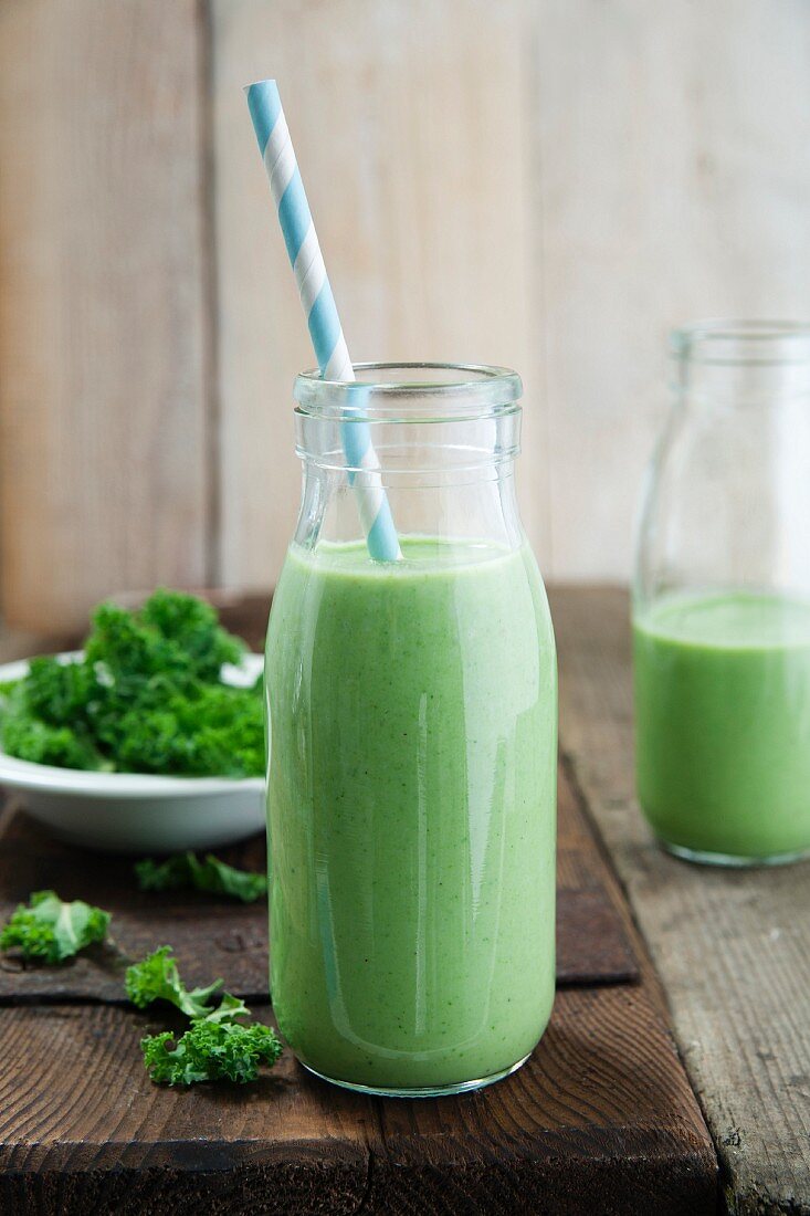 Kale and apple smoothie in a glass bottle with a straw