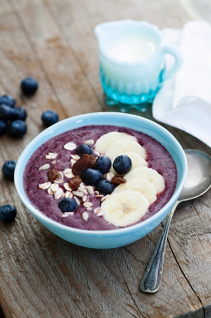 Smoothie-Schale aus Brombeere, Heidelbeere und Apfel mit Banane, Blaubeeren, Rosinen, Sonnenblumenkernen und Haferflocken