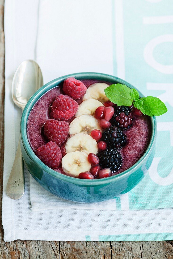 A smoothie bowl made from raspberries, blackberries, banana and strawberries garnished with raspberries, bananas, blackberries and pomegranate seeds