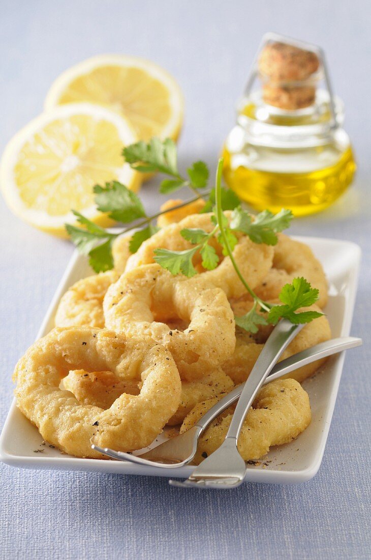 Gebackene Tintenfischringe auf Teller vor Zitronenhälften und Ölfläschchen