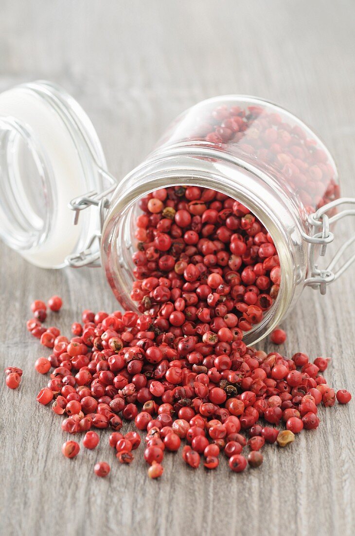 Pink peppercorns falling from an overturned jar