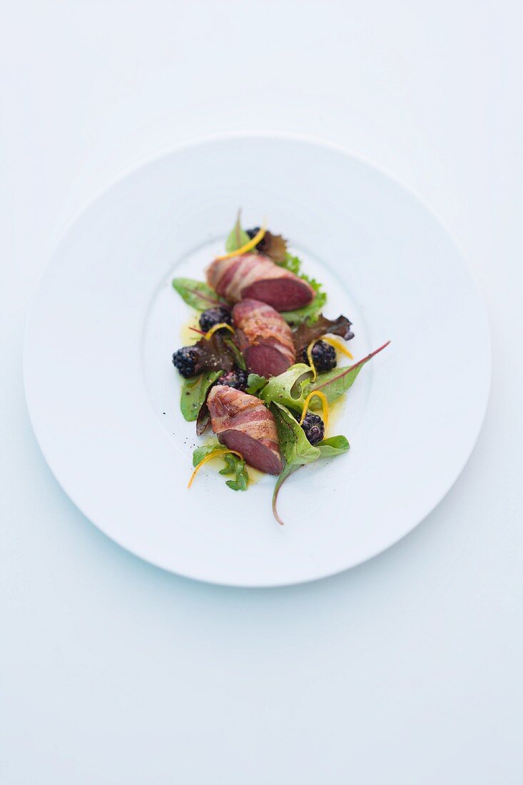 Wild rabbit wrapped in bacon on a mixed leaf salad with blackberries