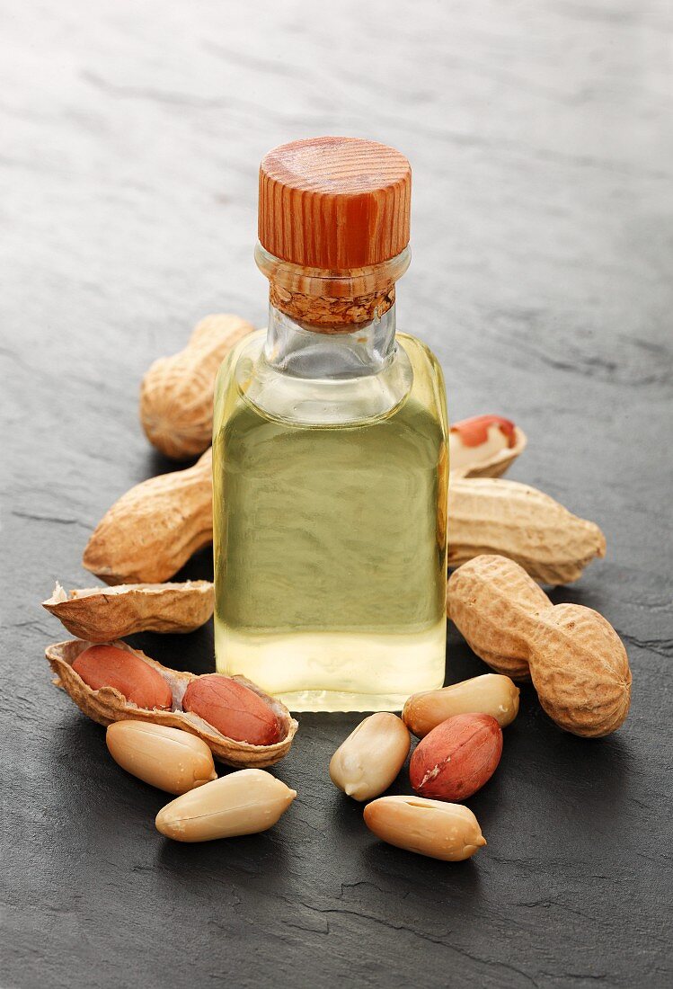 A bottle of peanut oil surrounded by peanuts