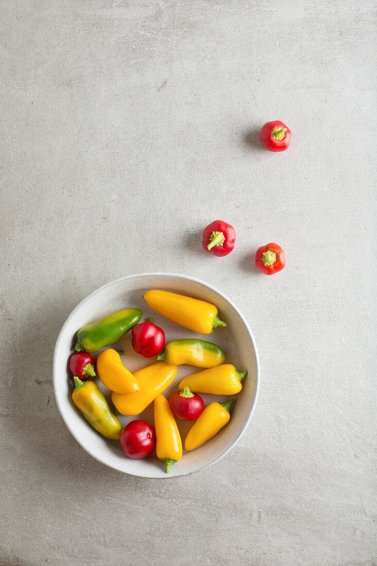 Red, yellow and green mini peppers in a bowl and next to it