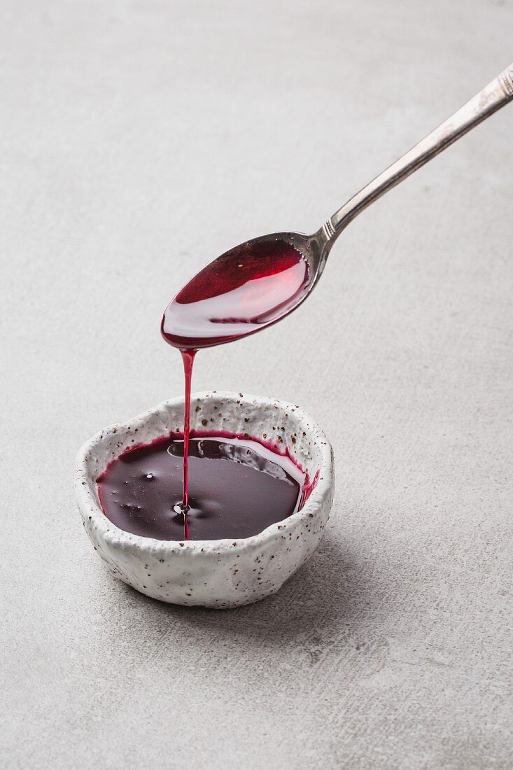 Pomegranate syrup dripping from a spoon into a bowl