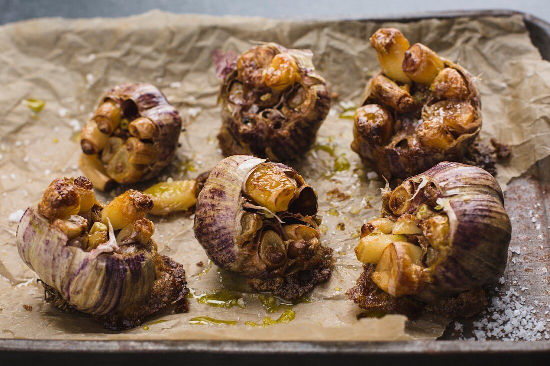 Roasted bulbs of purple garlic on baking tray with olive oil and salt