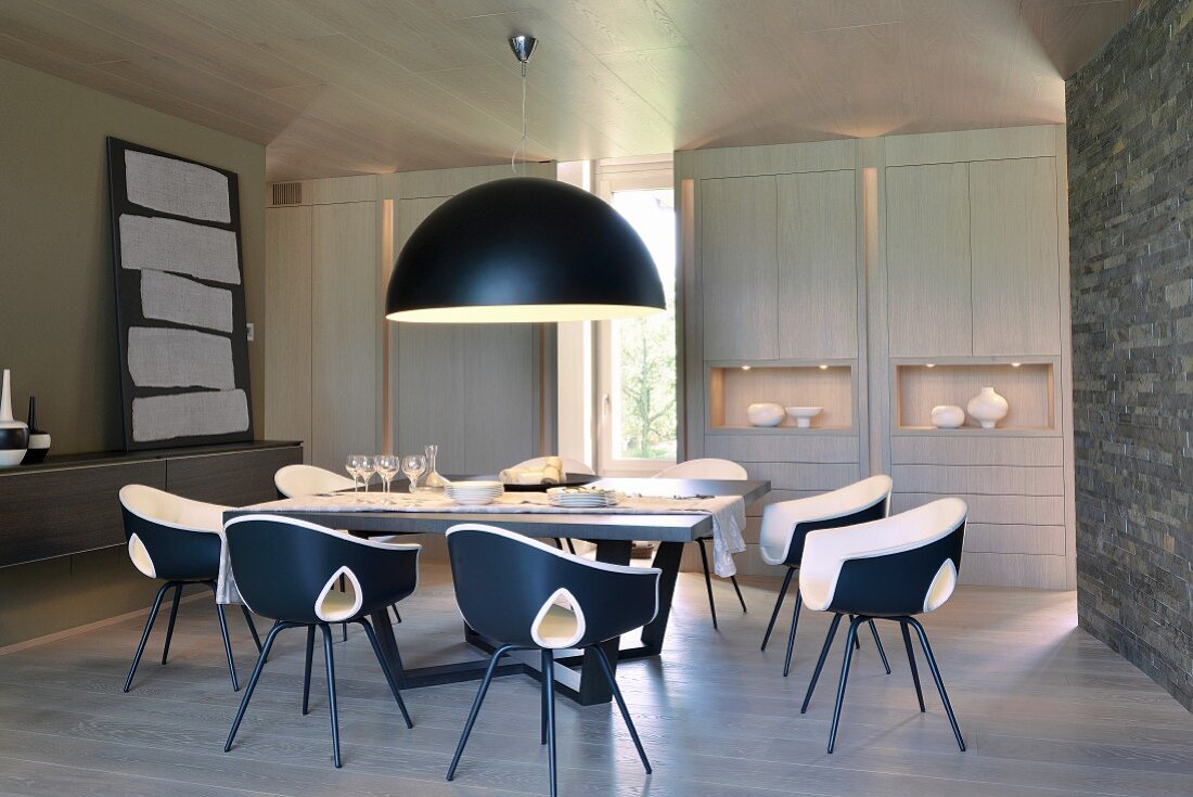 Pendant lamp with black hemispherical lampshade above dining set with designer chairs