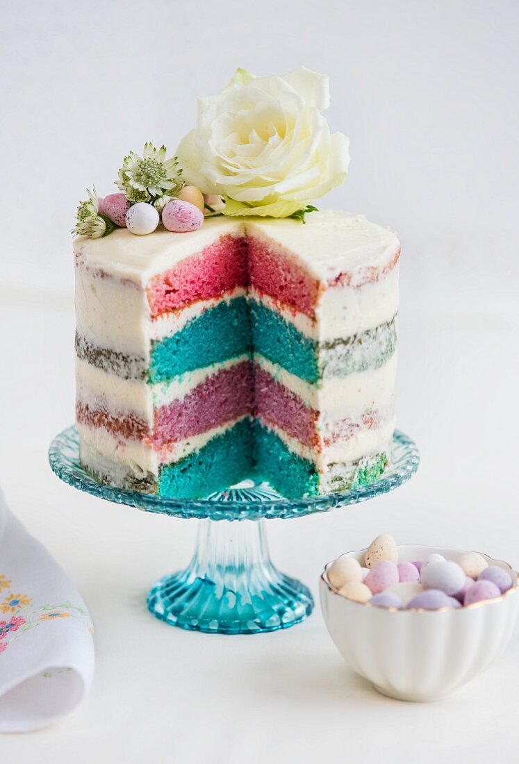 A four-layer rainbow cake with white frosting, Easter eggs and flowers (sliced)