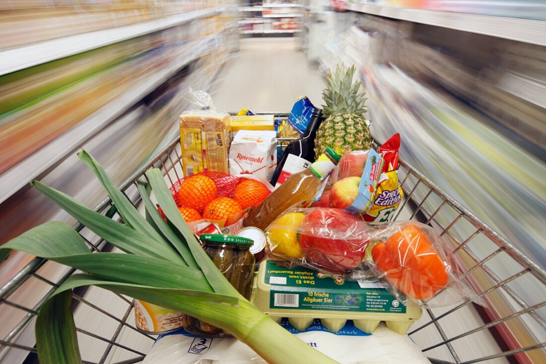 A full shopping trolley being pushed through a supermarket