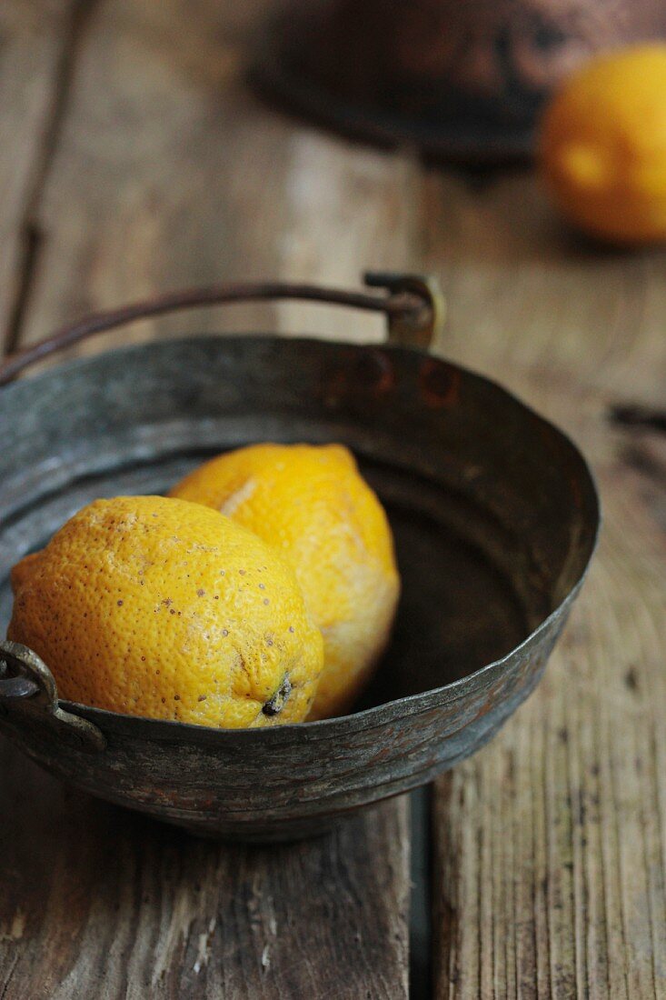 Lemons in a metal bowl on a rustic wooden surface