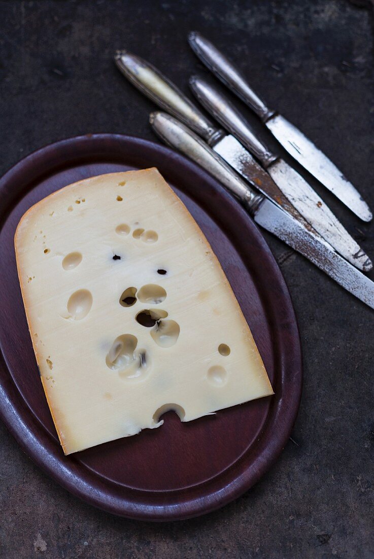 A piece of holey cheese on a plate next to old knives