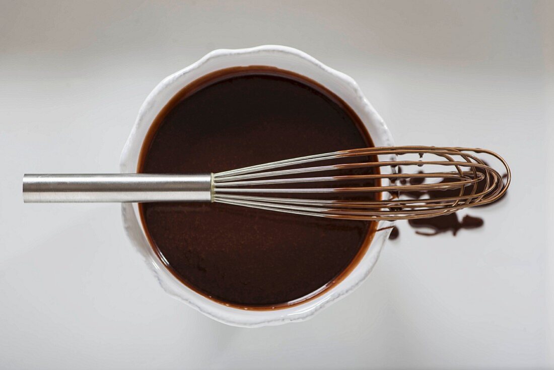 A bowl of chocolate ganache and a chocolate-covered whisk (seen from above)