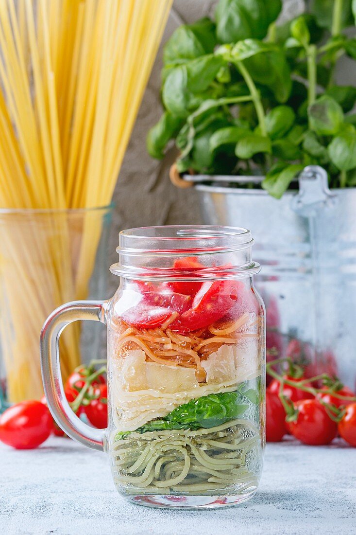 Colourful spaghetti with tomatoes, basil and cheese in a glass