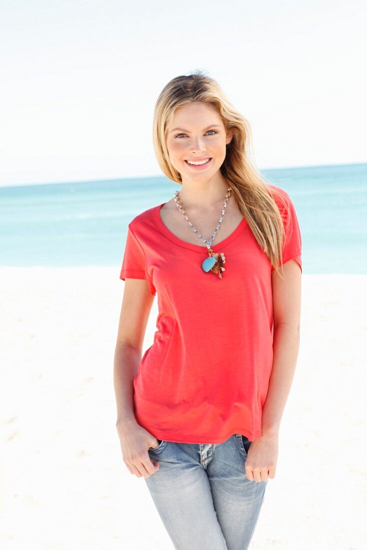 Junge Frau in rotem Shirt und Jeans am Strand