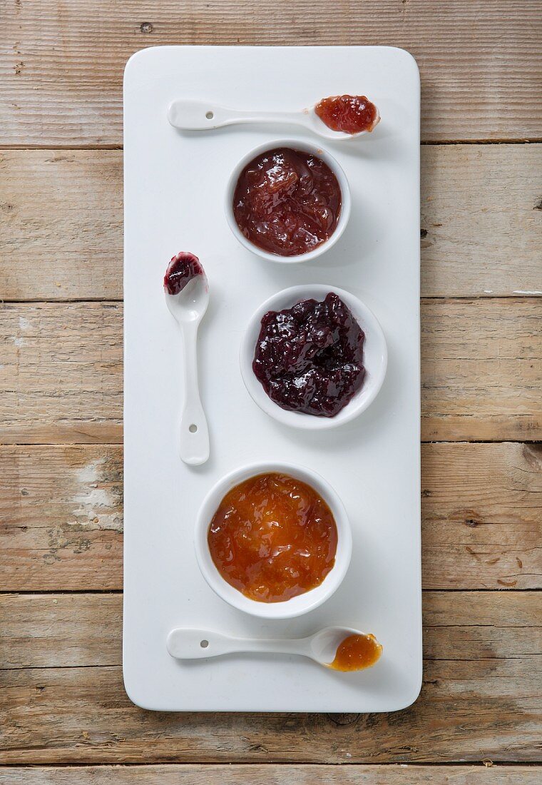 Three types of jam in bowls with spoons on a board