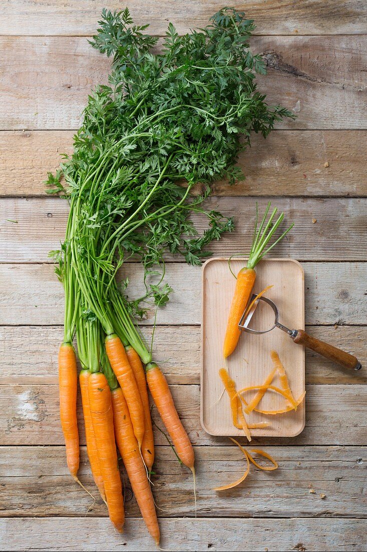 Fresh carrots next to a carrot on a chopping board with a vegetable peeler