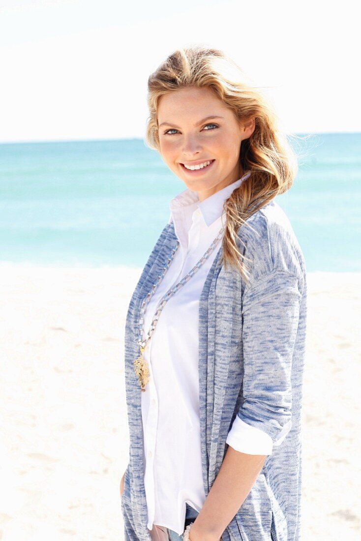 A young woman on a beach wearing a white blouse and a cardigan