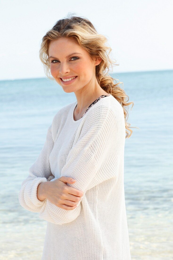 A young woman on a beach wearing a white knitted jumper