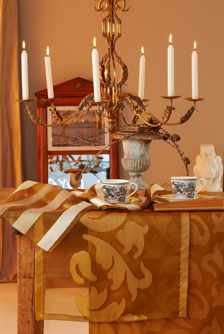 Autumnal dining table arrangement with gold runners and lit candles in chandelier