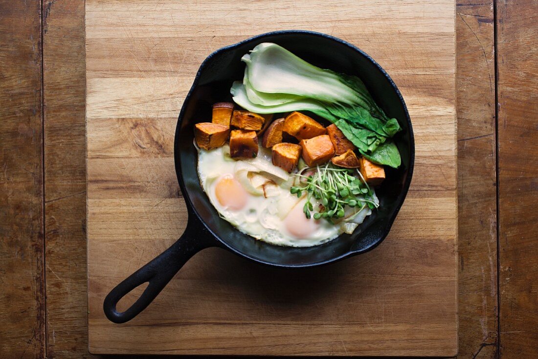 Organic fried eggs with bok choy, sweet potatoes and cress in a pan