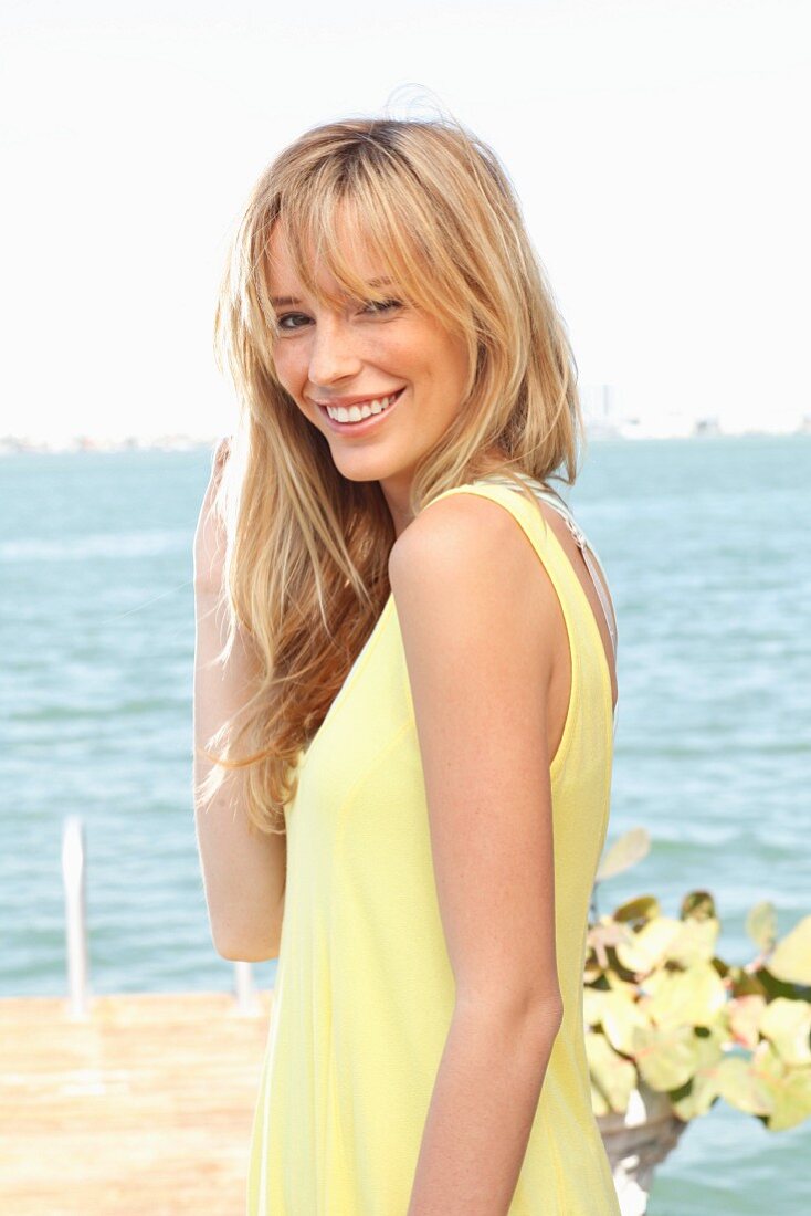 A young blonde woman by the sea wearing a yellow summer dress