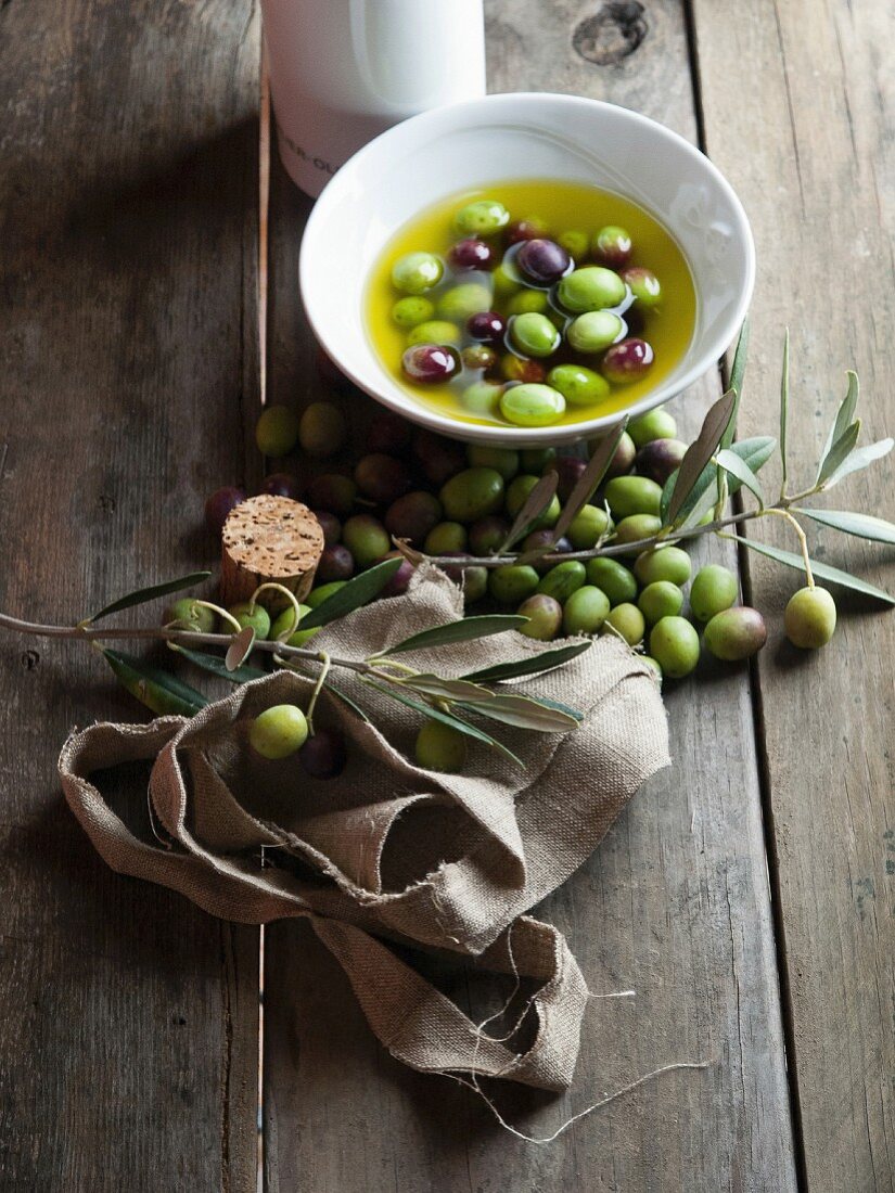 Olives and olive oil and a sprig of green olives on a rustic wooden table
