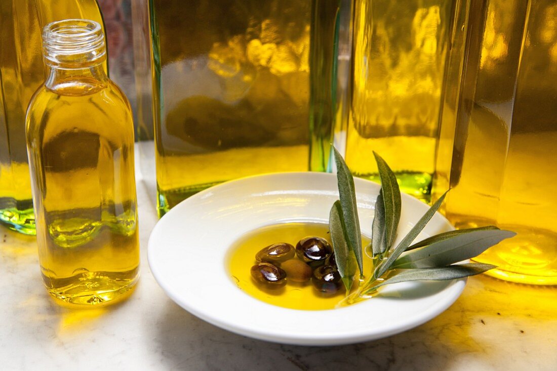 Stillleben mit Olivenölflaschen und Oliven mit Öl und Olivenzweig in weißem Teller