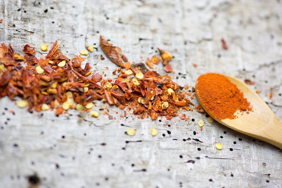 Chilli powder on a wooden spoon and chilli flakes on a wooden surface