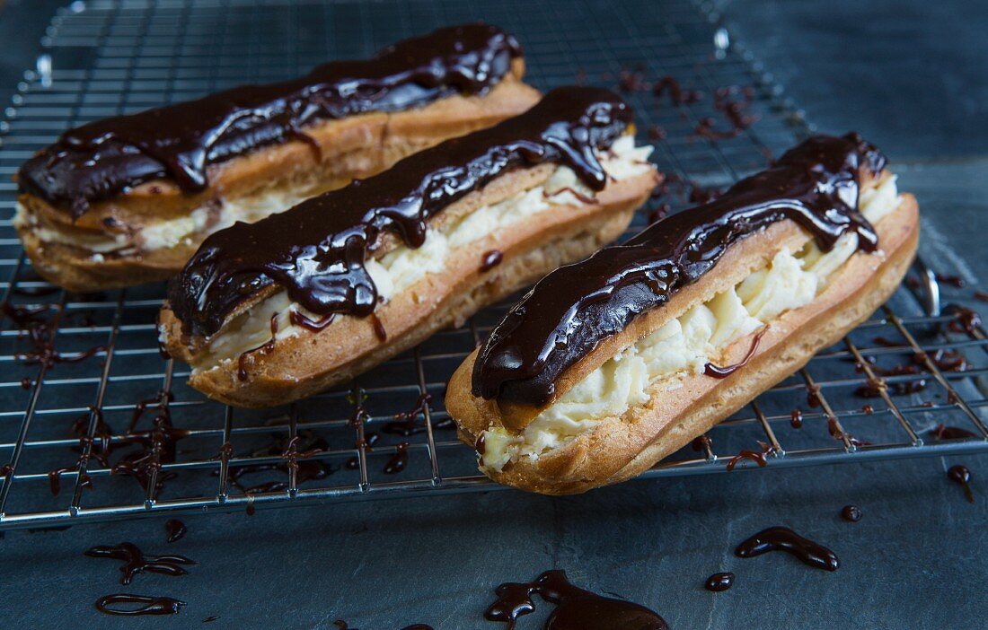 Chocolate eclairs filled with cream and topped with chocolate glaze on a wire rack