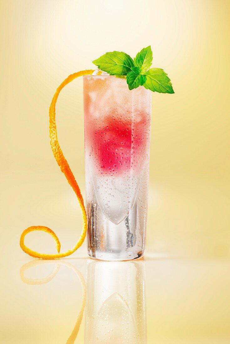 Pink cocktail glass garnished with orange zest on a yellow surface