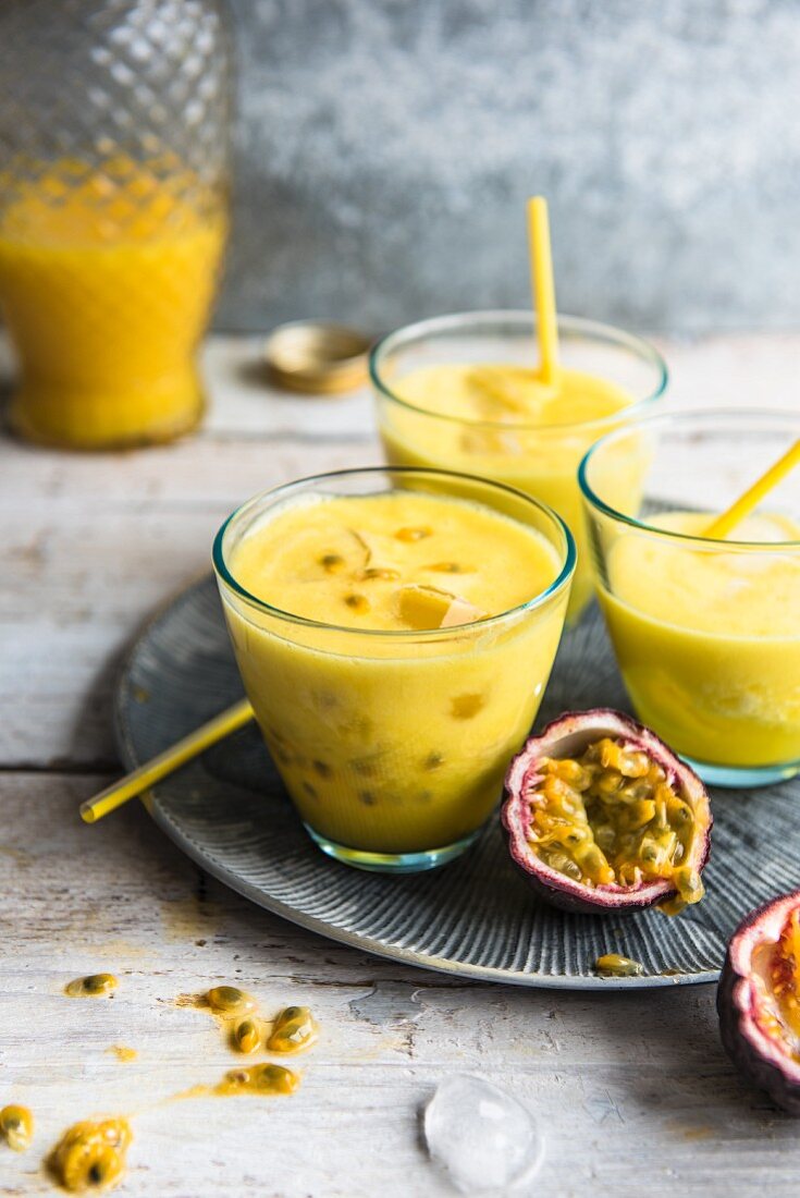 Drei Smoothies mit Passionsfrucht und Strohhalmen auf grauem Metallteller