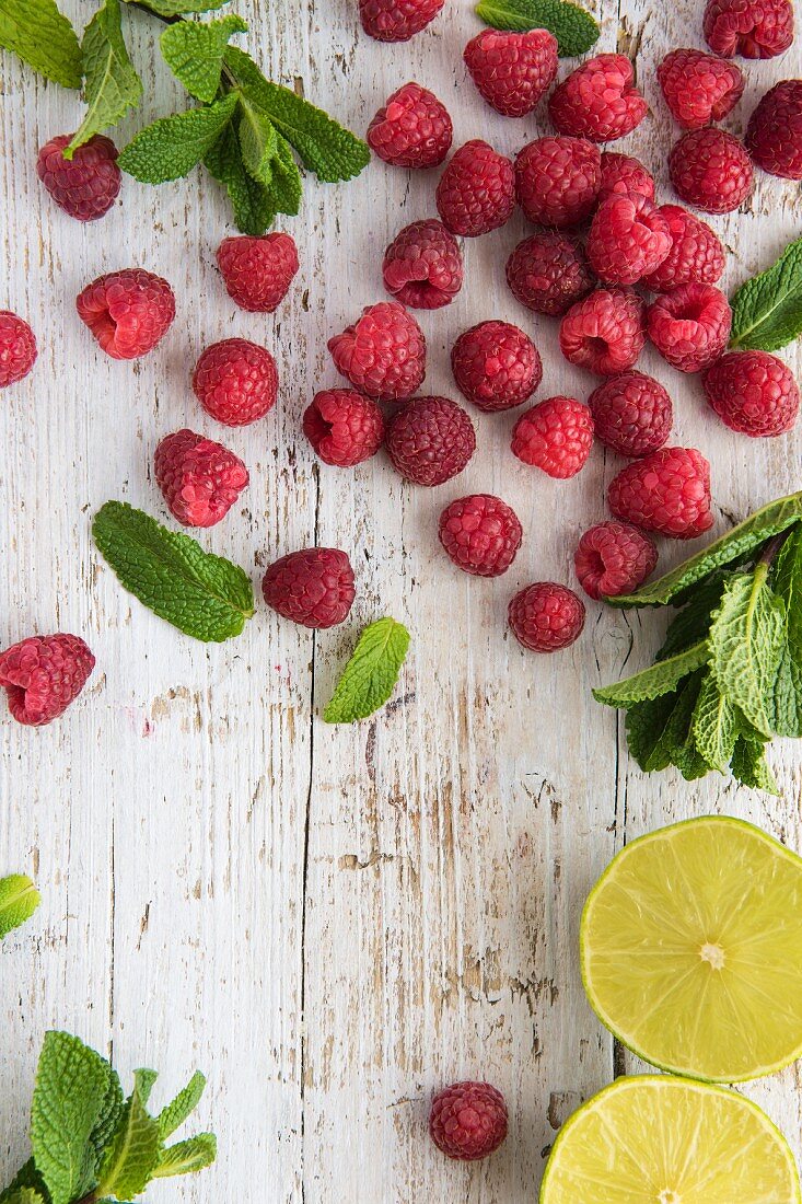 Fresh raspberries, mint and lime on a white wooden board (seen from above)