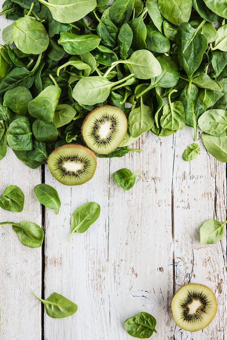 Spinach leaves and kiwis on a white wooden board (seen from above)