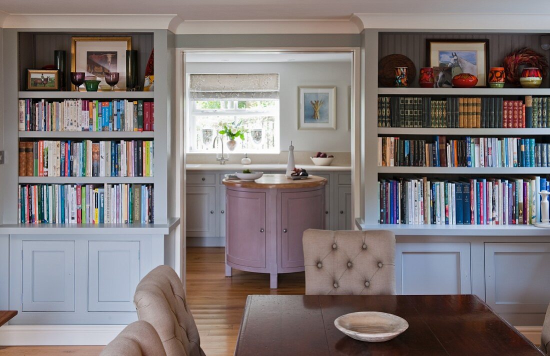 View from dining room with bookcases into rustic kitchen with pastel panelled cabinets
