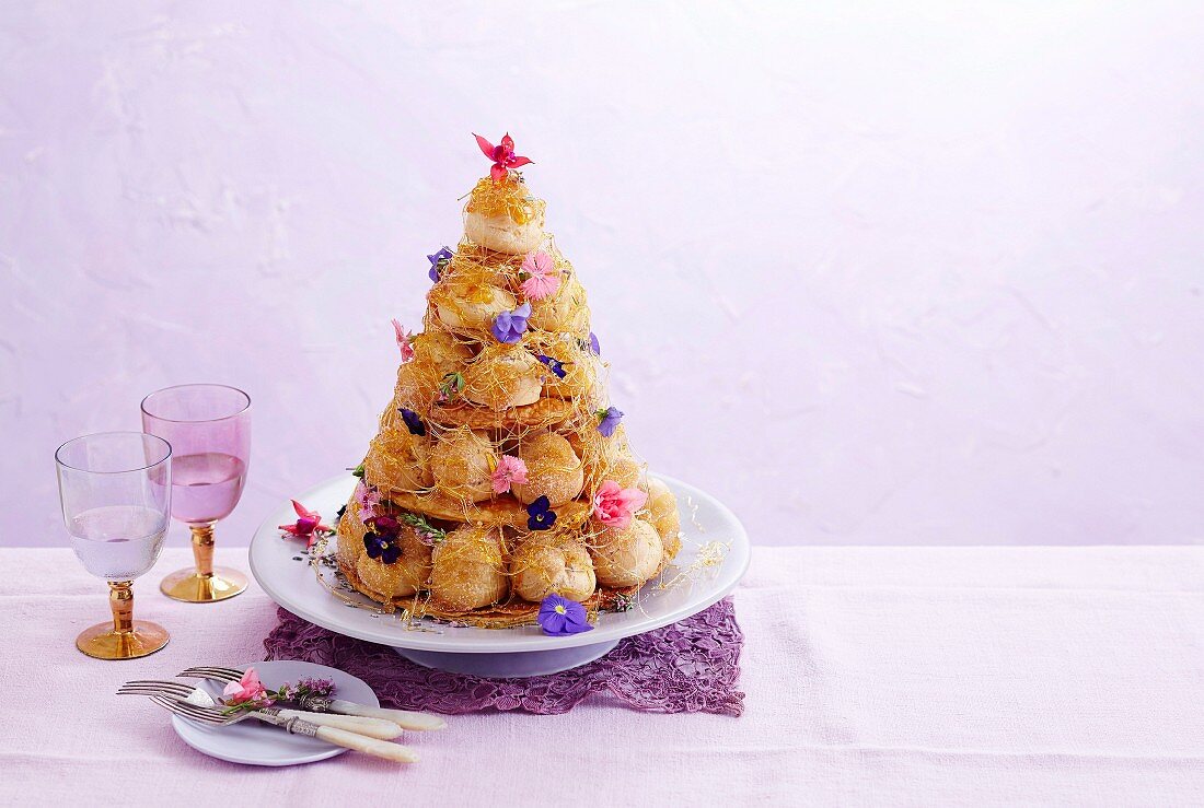 Croquembouche (French cake made of cream puffs) with caramel and edible flowers
