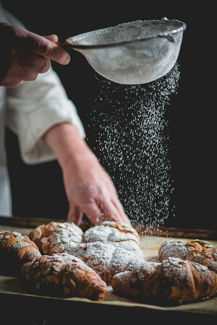 Croissants being dusted with icing sugar