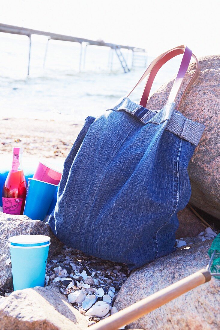 Tasche aus Jeansstoff und bunte Getränkebecher am Strand