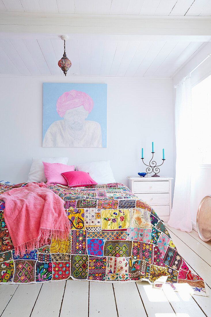 Brightly embroidered bedspread on bed in white bedroom