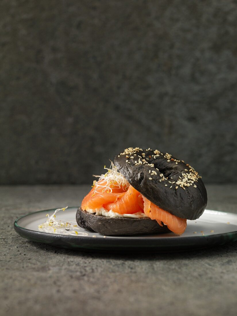 A black sesame seed bagel with smoked salmon, cream cheese and bean sprouts
