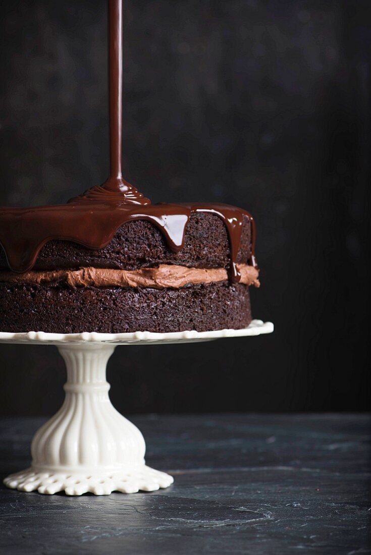 Chocolate icing being poured over a chocolate cake