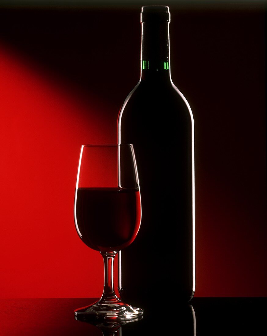 Umrisse von Glas und Flasche Rotwein vor dunklem Hintergrund