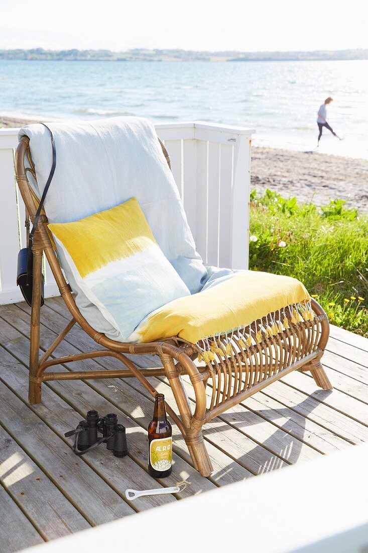 Rattansessel mit gelb-weißen Kissen auf einer Strandterrasse