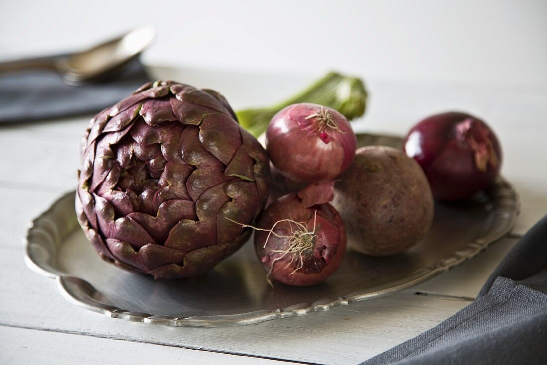 An arrangement of vegetables with an artichoke, onions and beetroot on the tray