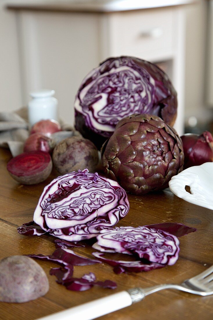 An arrangement of vegetables featuring artichokes, beetroot and red cabbage on a kitchen table