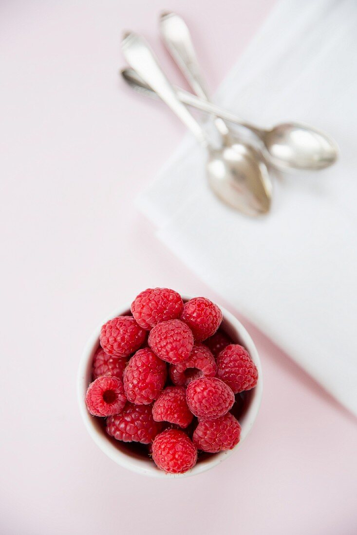 Raspberries in a white bowl on a pink tablecloth